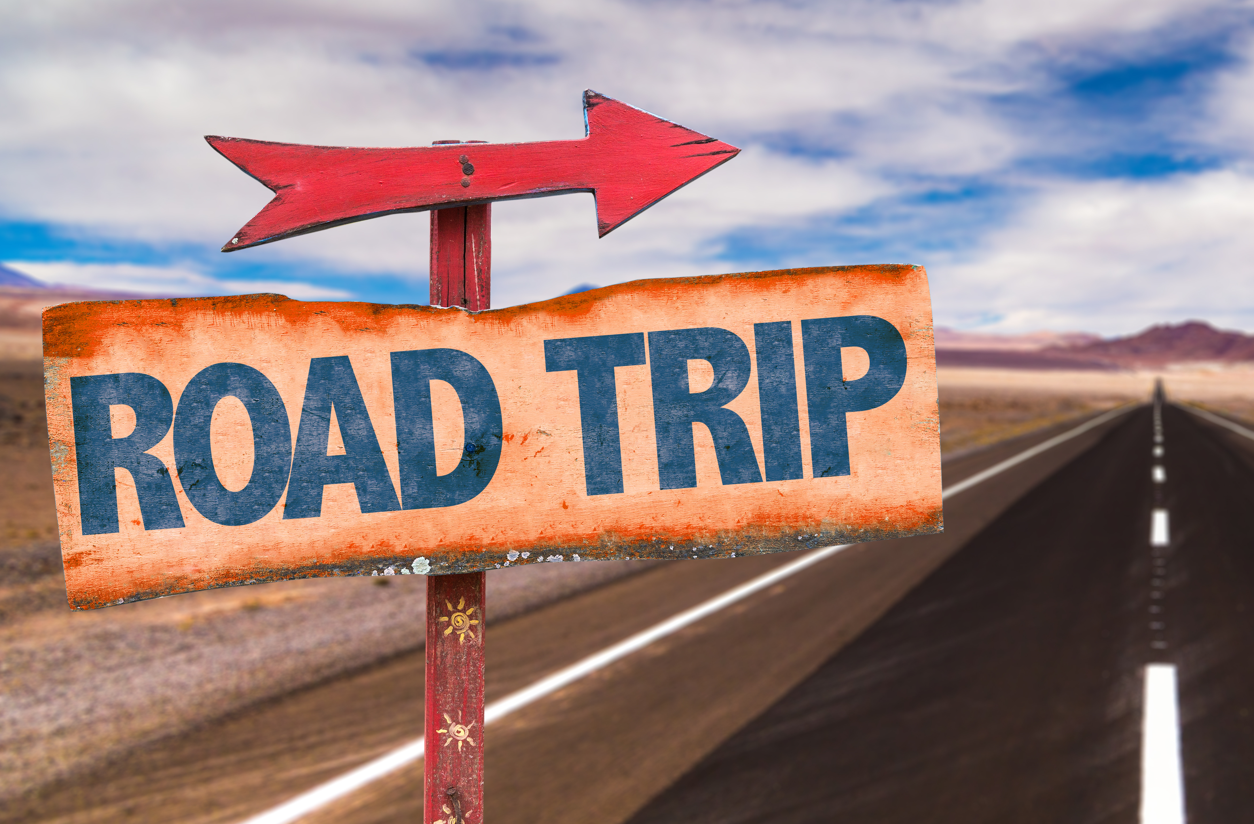 Road trip sign with arrow pointing along a long open highway through desert landscape